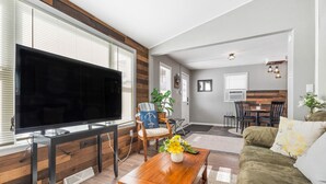 Un soggiorno moderno con una grande TV a schermo piatto, pareti rivestite in legno, una zona pranzo e un angolo salotto accogliente con divano e tavolino.