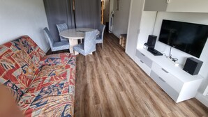 A compact living space with a sofa, a dining table with chairs, a TV, and a cabinet.