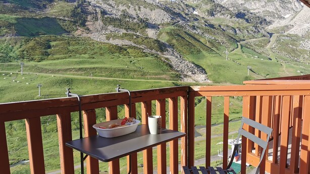 A balcony with a table, a chair, and a view of green hills and mountains.