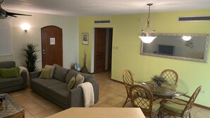 Uma sala de estar com sofá, mesa de jantar com cadeiras, ventilador de teto e espelho fixado na parede.