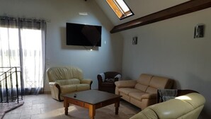 Un soggiorno con divano, poltrona e tavolino. C'è una TV montata a parete e una finestra con tende.
