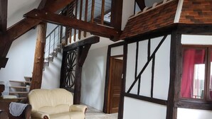 Una stanza con soffitto alto, travi in legno a vista, una grande ruota di legno e un divano in pelle beige.