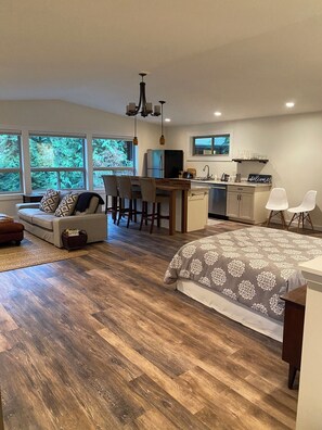 Relax in this open-plan living space with a kitchen area, sofa, and dining table, offering a view of the outdoors.