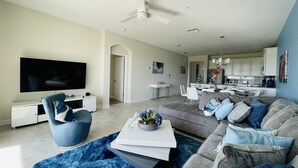 A modern living room with a flat-screen TV, a blue armchair, a grey sofa with blue cushions, and a dining area in the background. - LUXURY RESORT & GOLF CONDO MIN CLOSE TO DISNEY (Four Corners)