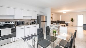 A modern kitchen with stainless steel appliances, a dining area with a glass table and chairs, and a living area with a sofa and a coffee table. - 2 Bedroom 2 Bath Beach 1 min Walk 8 People Keyless Free Parking Flex Check in (Sunny Isles Beach)
