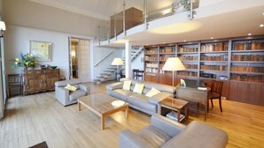 Un'ampia zona giorno dal design moderno, con un divano grigio, un tavolino in legno e una libreria piena di libri.