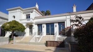 Una casa bianca a due piani con piscina, veranda coperta e un piccolo giardino.