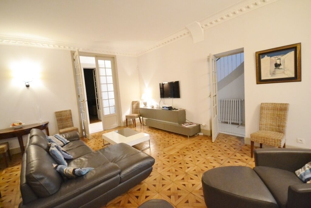 A living room with a sofa, armchairs, a coffee table, and a TV. There is a staircase leading to another room.