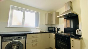 Eine kompakte Küche mit Waschmaschine, Mikrowelle, Backofen und einem Fenster mit Jalousien.