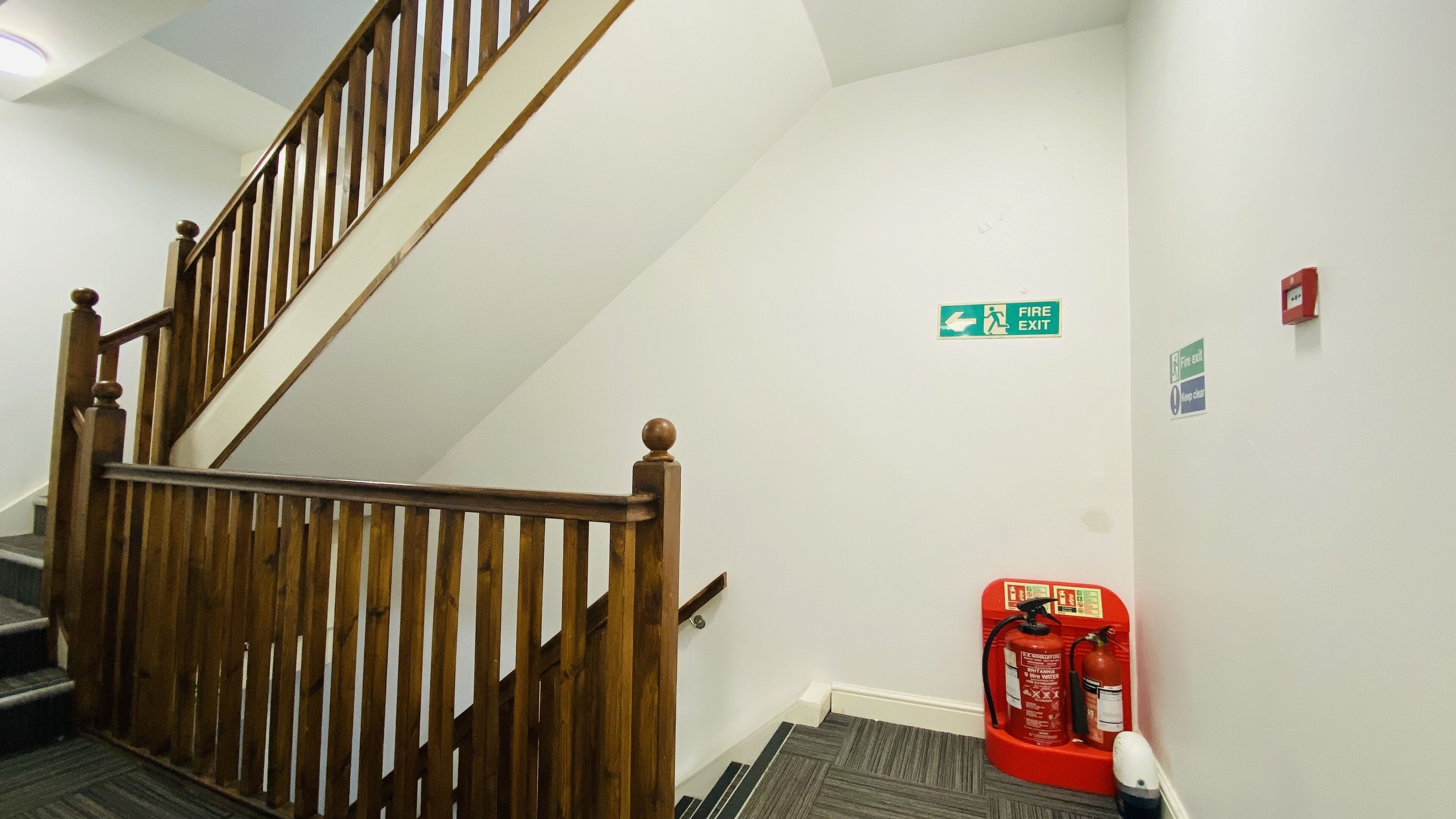 A staircase with wooden railings, a fire exit sign, and a fire extinguisher on the wall.