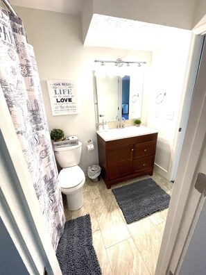 A bathroom with a toilet, sink, mirror, and a shower curtain with a cityscape design.