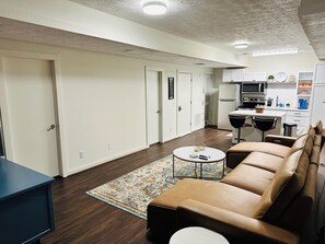 A modern living room with a sofa, a coffee table, and a kitchen area with a microwave and refrigerator.
