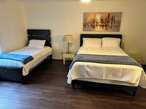 Two single beds with dark headboards, a bedside table with a lamp, and a cityscape painting on the wall.