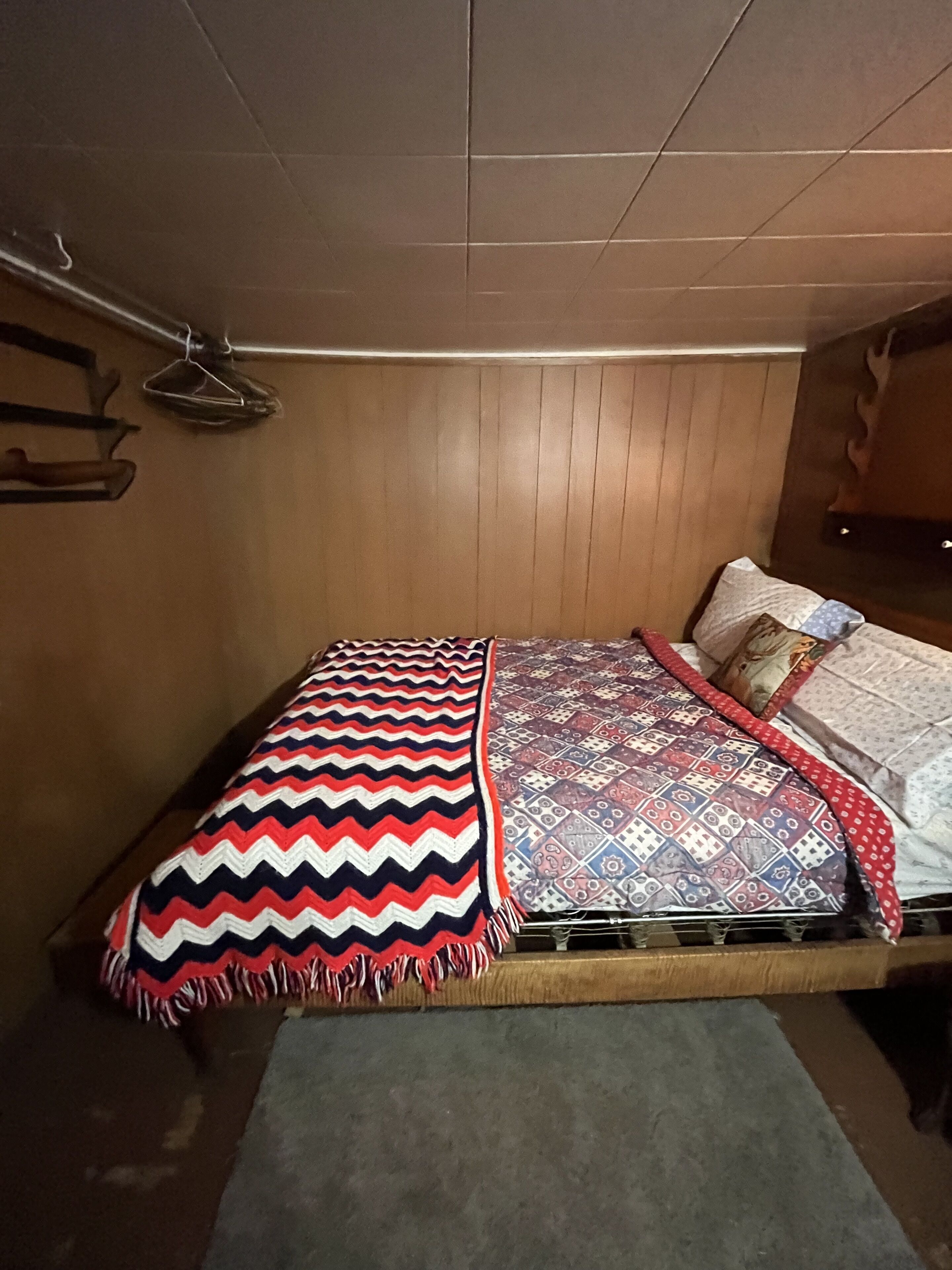 Ein Schlafzimmer mit einem hölzernen Bett, einer gemusterten Decke und einem Nachttisch mit einer Lampe.