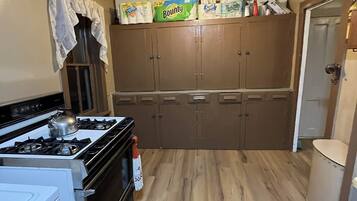 A compact kitchen with a gas stove, oven, and a refrigerator. There are wooden cabinets and a ceiling fan.