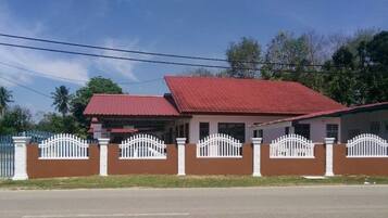 A two-story house with a red roof, white picket fence, and a paved driveway.