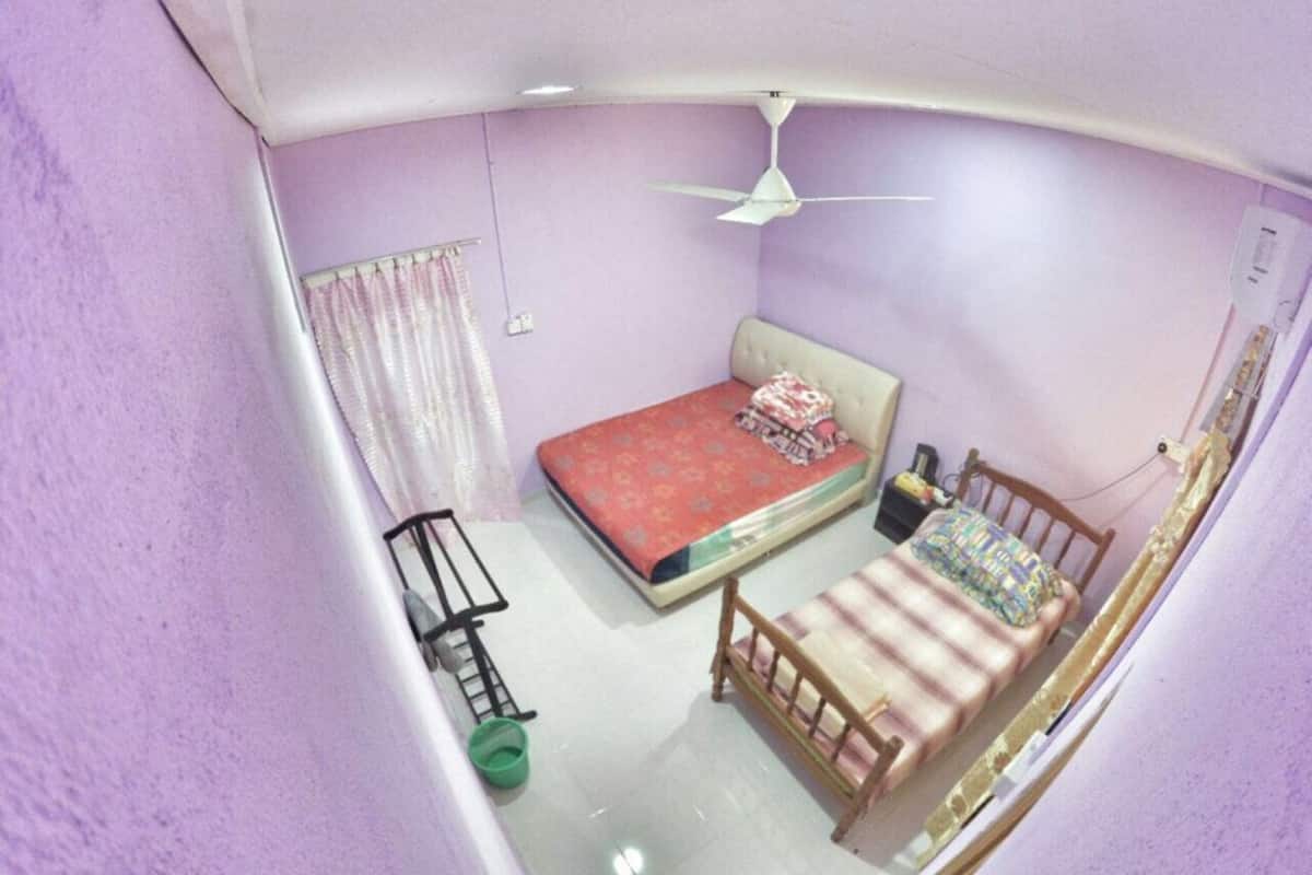 A small, single-bed room with a ceiling fan, a bedside table, and a green bucket.