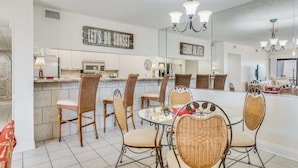 A spacious kitchen with a dining area, featuring a large island, wicker chairs, and pendant lighting. - Moondrifter #305 2 BR - Free Beach Chairs! (Panama City Beach)