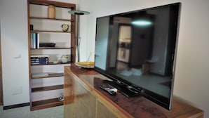 A living room with a flat-screen TV on a wooden stand, a bookshelf with various items, and a floor lamp. - Bra Luxury Rooms & Apartment (Verona)