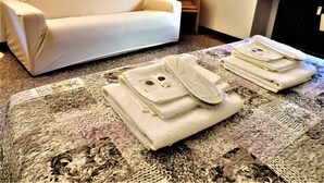 A hotel room with a white sofa, a small wooden chair, and a table with folded towels and a hairdryer. - Bra Luxury Rooms & Apartment (Verona)