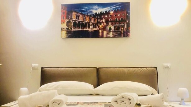 A hotel room with a bed, two pillows, a neatly folded towel, and a painting of a cityscape on the wall. - Bra Luxury Rooms & Apartment (Verona)