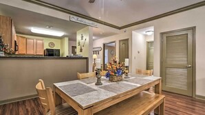 A dining area with a wooden table and chairs, a kitchen in the background, and a closed door. - Close To It ALL with Indoor & Outdoor Pools (Pigeon Forge)