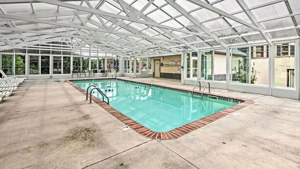 An indoor swimming pool with a glass ceiling, surrounded by lounge chairs and a concrete floor. - Close To It ALL with Indoor & Outdoor Pools (Pigeon Forge)