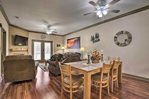 A living room with a wooden dining table, two ceiling fans, a TV mounted on the wall, and a fireplace.