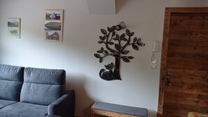 Una sala de estar con un sofá gris, un banco de madera pequeño y un árbol decorativo colgado en la pared.