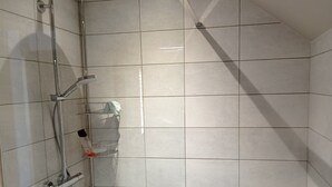 Un pequeño espacio de ducha con azulejos, equipado con ducha de mano y cabezal de ducha manual.