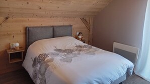 Un dormitorio con techo de madera, una cama con colcha estampada, una mesita de noche con lámpara y una ventana con cortinas.
