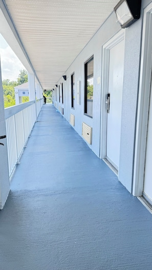 A covered corridor with a blue floor, white walls, and doors on one side. - Westen Motel (Scooba)