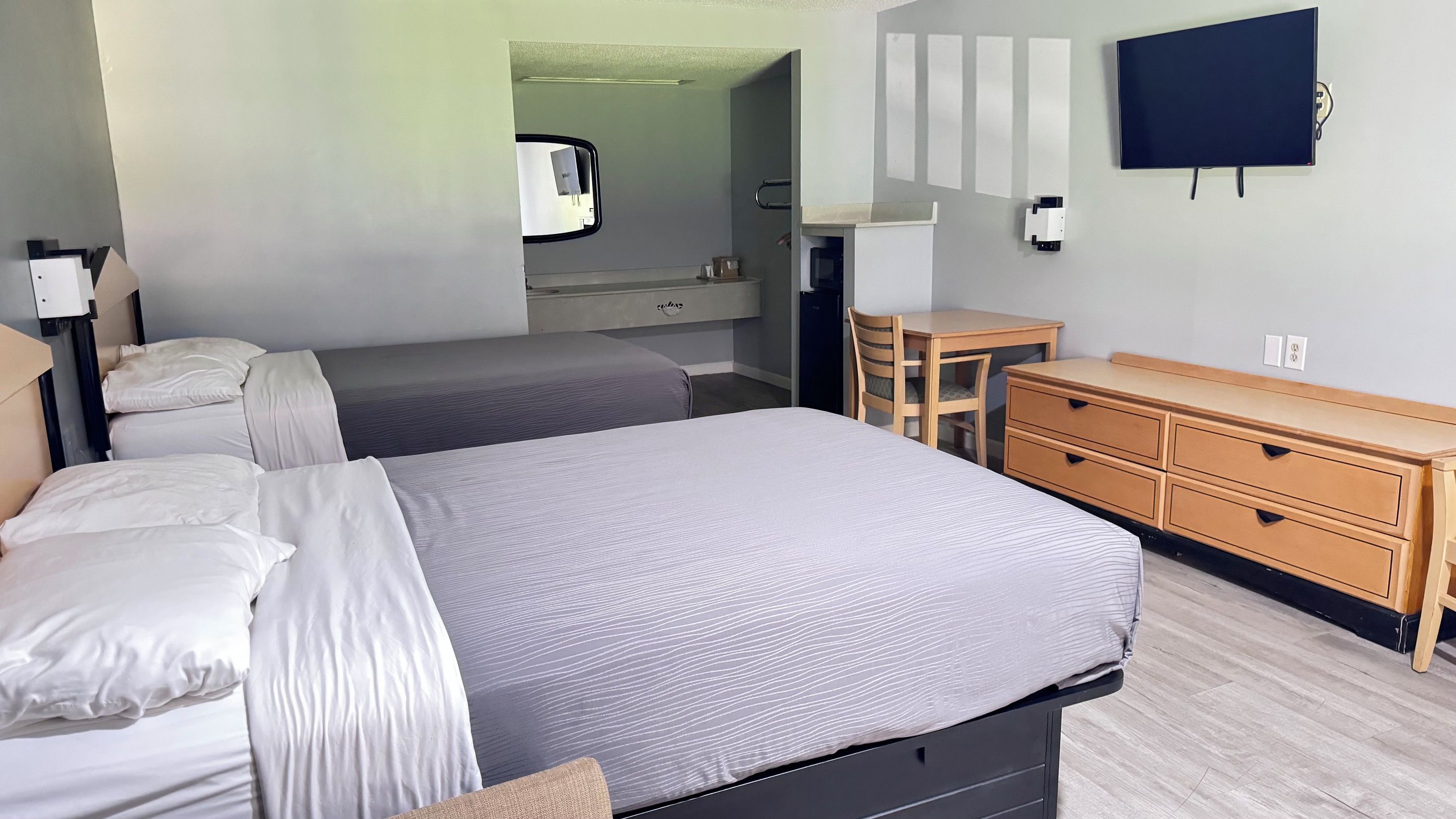 Habitación de hotel con dos camas, un escritorio, una silla, un aparador y un televisor de pantalla plana montado en la pared.