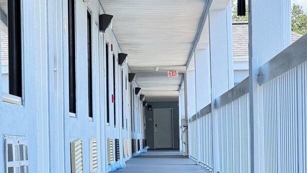 A long, covered corridor with a series of doors on one side and a railing on the other. - Westen Motel (Scooba)