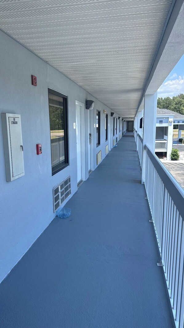 A long corridor with a covered walkway, fire extinguishers, and a fire alarm on the wall. - Westen Motel (Scooba)