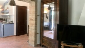 Una stanza con un armadietto in legno, una televisione su un mobile e una zona cucina visibile attraverso una porta aperta.