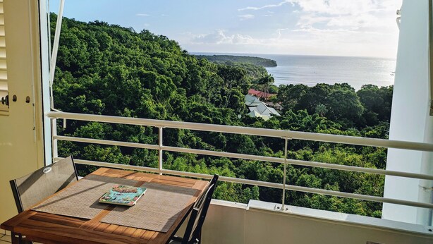 Un balcón con vistas a un paisaje costero, una mesa de madera con una revista y un toldo a rayas.