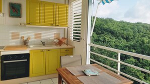 Una cocina con armarios amarillos, un horno negro y una ventana con vistas a un área boscosa.