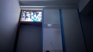 Une pièce avec un plafond en pente, une fenêtre donnant sur les arbres et un mur décoré d’un ruban adhésif bleu.