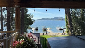 En utsikt från en inglasad veranda med utsikt över en sjö med båtar, en brygga och en gräsyta med blommor.