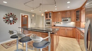 Una cocina moderna con armarios de madera, electrodomésticos de acero inoxidable y una isla central con taburetes de bar.