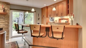 Una cocina moderna con armarios de madera, una isla central con taburetes de bar, iluminación colgante y vistas al exterior.