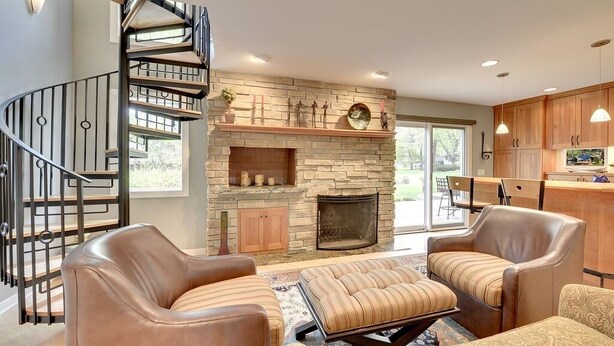 Una sala de estar moderna con chimenea de piedra, sofás de cuero, una mesa de centro y una escalera en espiral.