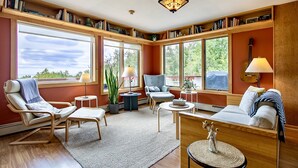 A spacious living room with large windows, a fireplace, and a bookshelf filled with books.