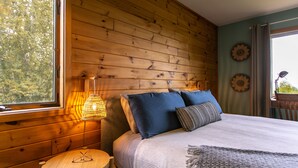 A wooden-paneled room with a bed, a small table, and a window with a view of trees.