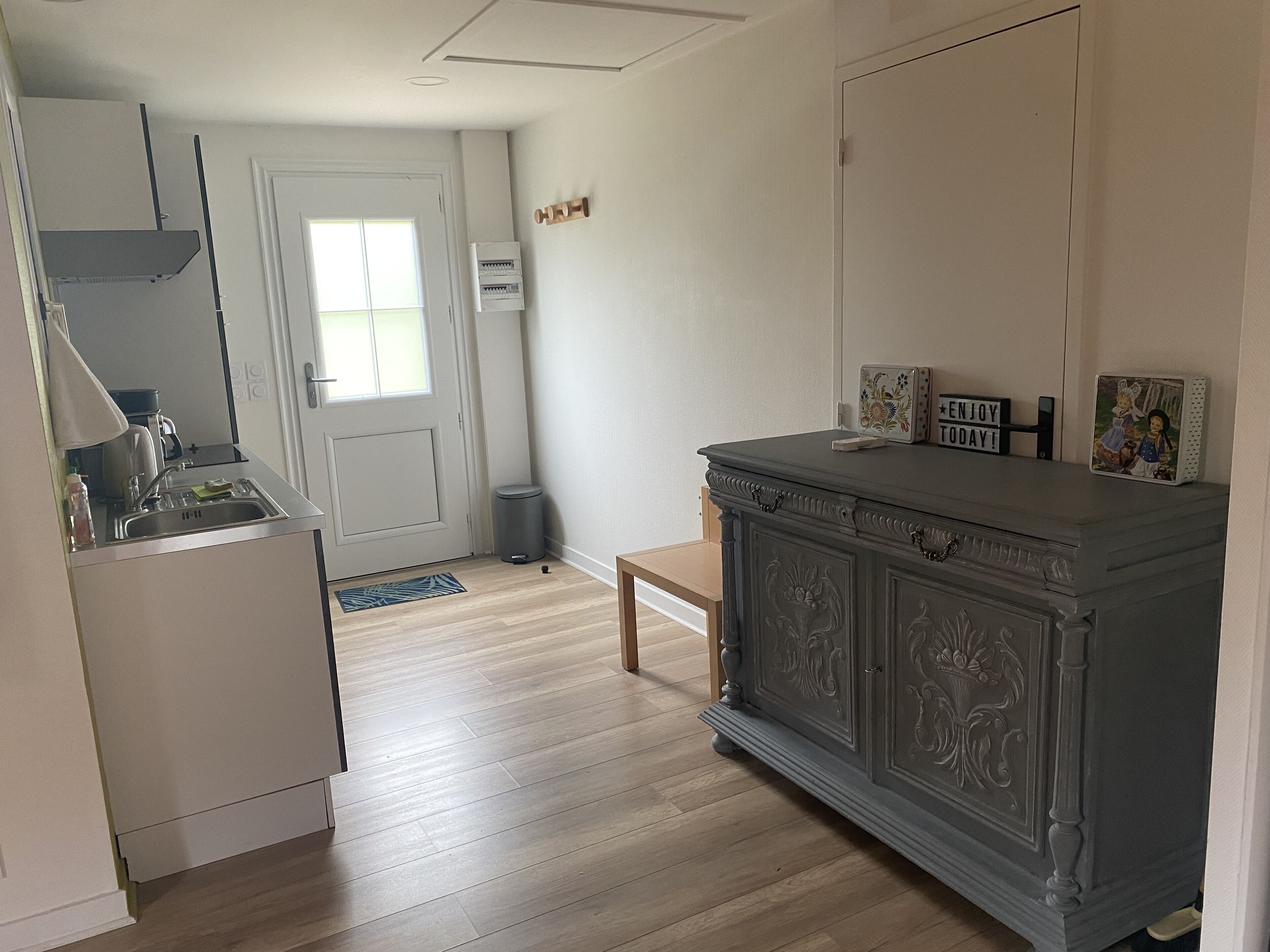 Une cuisine moderne dotée d’un four encastré, d’un évier et d’une fenêtre. On y trouve un meuble gris orné de motifs décoratifs et un petit tapis sur le sol.
