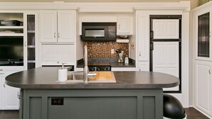 A kitchen with white cabinetry, a central island, a microwave, and a sign that reads "LET'S DO SUNSET". - Large Glamper w/ Hot Tub and full bathroom-sleep 6 (Capon Bridge)