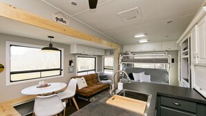 A compact RV interior with a kitchenette, dining area, and a bunk bed. - Large Glamper w/ Hot Tub and full bathroom-sleep 6 (Capon Bridge)