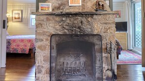 Une cheminée en pierre avec un paravent, des poutres en bois et un tableau encadré au-dessus.