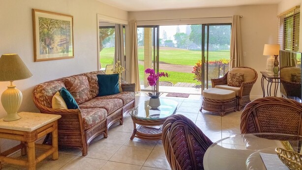 Un salon comprenant un canapé, des fauteuils, une table basse et donnant sur un jardin grâce à une porte vitrée.